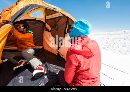 Man and woman setting up tent before camping in winter in White Mountains, New Hampshire, USA Stock Photo
