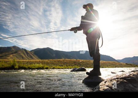 Sun shining behind fisherman fishing in Madison River, Montana, USA Stock Photo