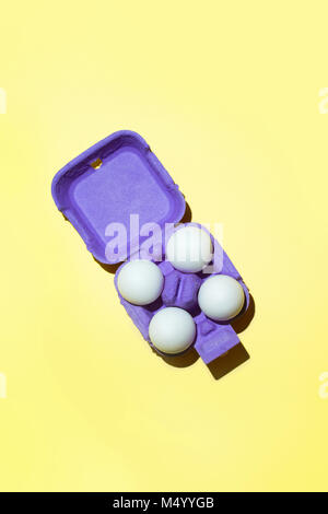 White four eggs in violet the package on yellow background. Top view. Stock Photo