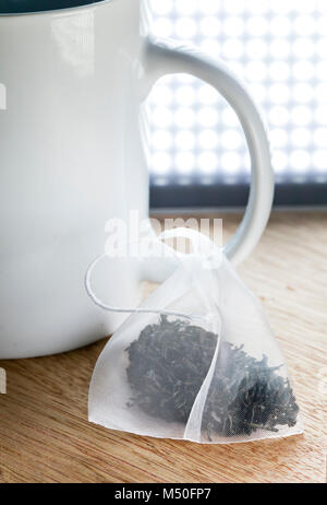 Single bag of elite tea in silk fabric packing and tea mug on a wooden background Stock Photo