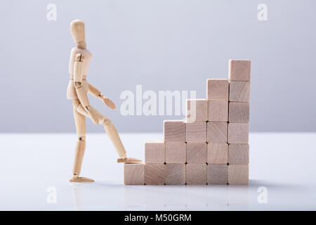 Side View Of A Wooden Figure Climbing Staircase On White Background Stock Photo