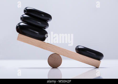 Black Stones Balancing On Wooden Seesaw Over The White Background Stock Photo