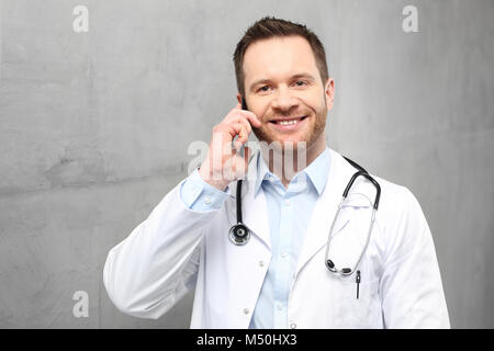 doctor is talking on the phone. A handsome doctor dressed in a white overalls stands in a clinic and is talking on the phone Stock Photo