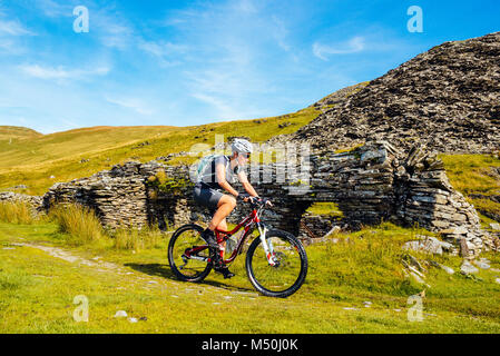 Female mountain biker passing quarry ruins at Walna Scar Quarries in the English Lake District Stock Photo