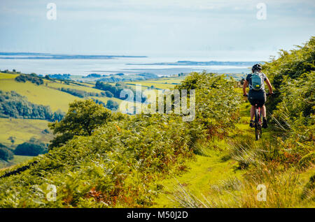 Female mountain biker on trail above the River Lickle in the English Lake District with Morecambe Bay in the distance Stock Photo