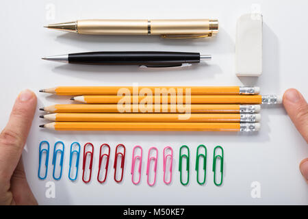 Person's Finger Arranging The Pencils With Row Of Pins Rubber And Pen On White Background Stock Photo