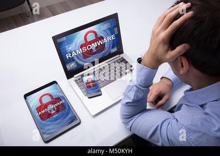 Worried Businessman With Cellphone, Digital Tablet And Laptop With Encrypted Text On The Screen Stock Photo