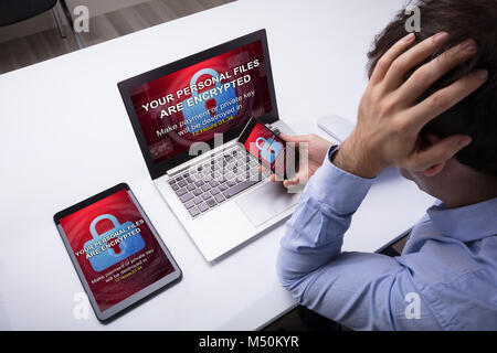 Worried Businessman With Cellphone, Digital Tablet And Laptop With Encrypted Text On The Screen Stock Photo