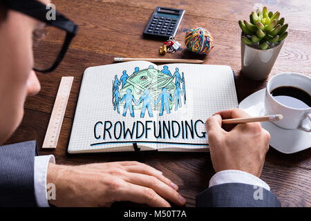 Man Drawing Crowdfunding Concept In Notepad At Desk Stock Photo