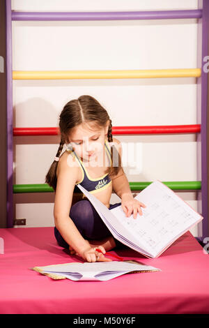 Little caucasian 6-8 years old girl doing one's lessons at the gym Stock Photo