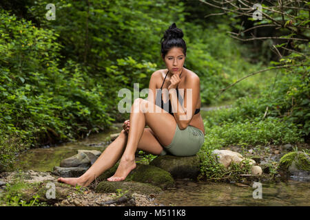 Young woman sitting on a stone in stream Stock Photo