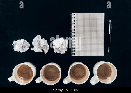 top view of blank notepad with crumpled papers and cups of coffee in row isolated on black Stock Photo