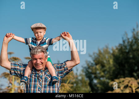 Grandfather carries grandson toddler boy on his shoulders Stock Photo