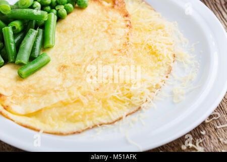 Homemade omelet with green beans and peas, filling with grated cheese, fresh breakfast on rustic wooden table Stock Photo