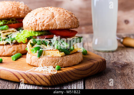 Egg omelet burger with  green beans and peas filling  on rustic wooden cutting board, delicious  vegetarian snack in rural style Stock Photo