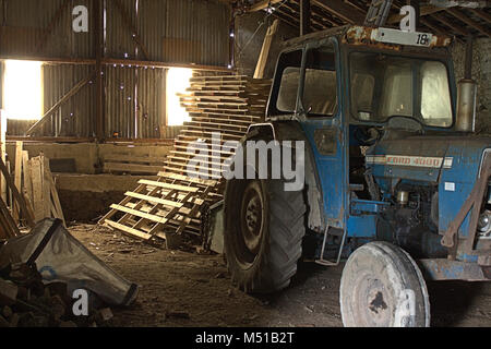 Ford Tractor being refurbished in a barn. Its early morning and the barn has sunlight streaming in through the windows. Stock Photo