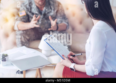 Female therapist listening to military patient and taking notes Stock Photo