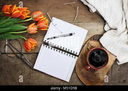 Overhead shot a bouquet of an open book or garden planner, glasses, coffee, sissors and flowers over a wood table top ready to plan an agenda. Flat la Stock Photo