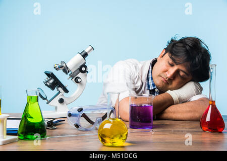Asian/Indian male scientist or doctor or science student experimenting with microscope and chemicals, laptop and smartphone in a lab Stock Photo