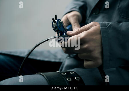 closeup of a young caucasian worker man, wearing a gray working coat, making a hole in a belt with a leather punch Stock Photo