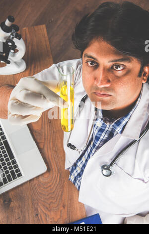 Asian/Indian male scientist or doctor or science student experimenting with microscope and chemicals, laptop and smartphone in a lab Stock Photo
