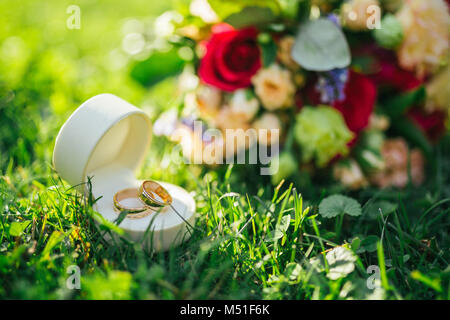 Wedding rings in a box lie next to a bouquet on the grass Stock Photo
