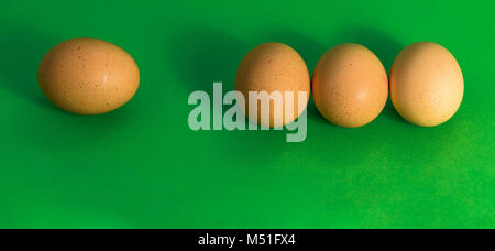 Abstract picture at Easter, three eggs lying close to each other and a single sad egg further away, on grass-green background, concept lonely Stock Photo