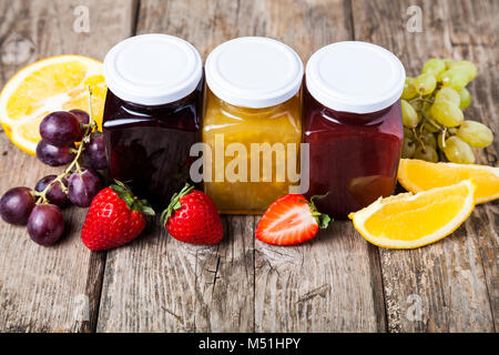 Three jars with jam on a wooden background. Delicious dessert and fresh fruits close-up. Stock Photo