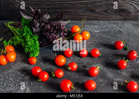 Fresh vegetables parsley greens cherry tomatoes and basil on a dark background on a table with a texture of gray concrete Stock Photo
