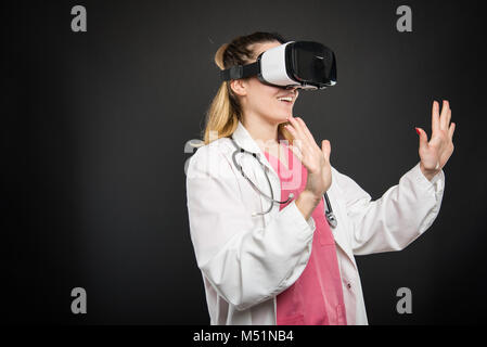 Female doctor wearing virtual reality glasses and gesturing on black background with advertising area Stock Photo