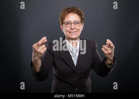 Business senior lady showing double fingers crossed on black background Stock Photo