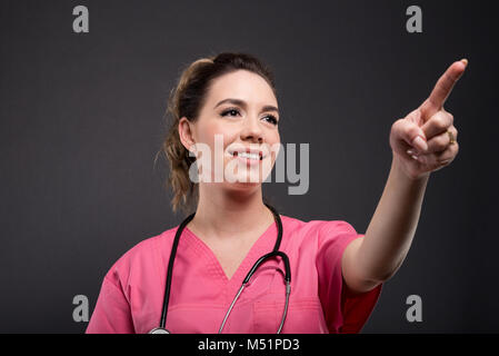 Portrait of beautiful young doctor using touchscreen with index finger on black background Stock Photo