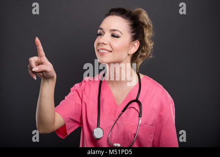 Portrait of beautiful young doctor using touchscreen with index finger and smiling on black background Stock Photo