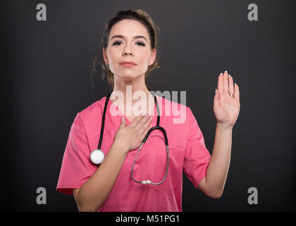 Portrait of beautiful young doctor taking oath on black background Stock Photo