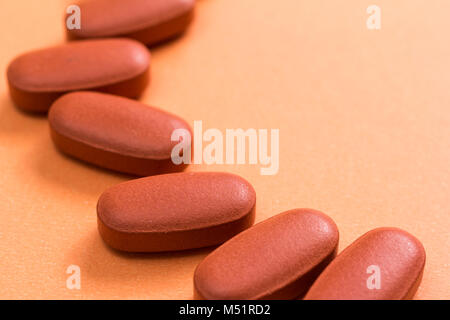 Heap of brown capsules on orange table. Stock Photo