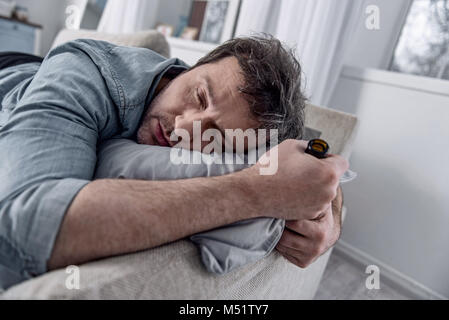 Drunk man holding a bottle while falling asleep on the sofa Stock Photo