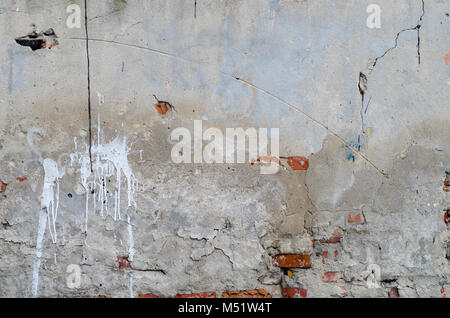 old grey concrete garage wall with red bricks, cracks and white spots abstract background Stock Photo