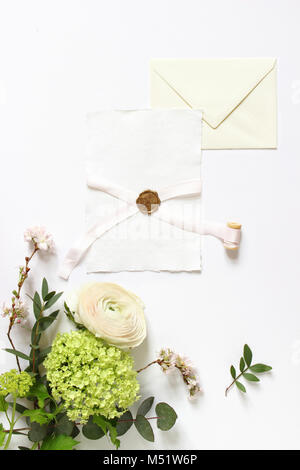 Feminine wedding, birthday desktop mock-ups. Blank greeting card with seal, ribbon and envelope. Eucalyptus branches, pink cherry tree blossoms and Persian buttercup flower. White table background. Flat lay, top view. Stock Photo