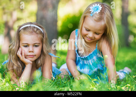 Two little sisters having fun in summer park while laying on lawn Stock Photo