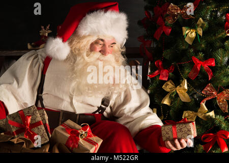 Santa putting gifts under Christmas tree in dark room Stock Photo