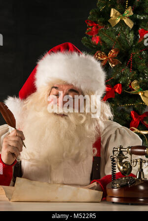 Portrait of Santa Claus answering Christmas letters using vintage tools - paper roll, feather pen, ink, wooden retro phone Stock Photo