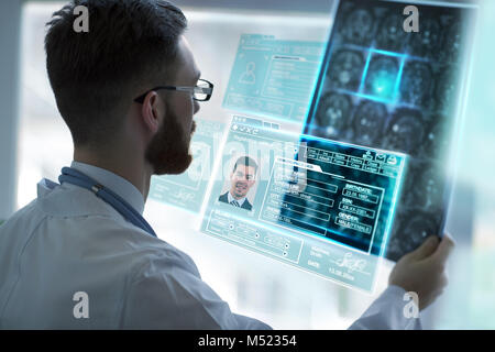 Closeup portrait of intellectual man healthcare personnel with white labcoat, looking at brain x-ray radiographic image, ct scan, mri, clinic office b Stock Photo