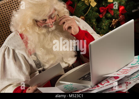 Santa Claus working on computer reading emails and paper letters from children from all over the world Stock Photo