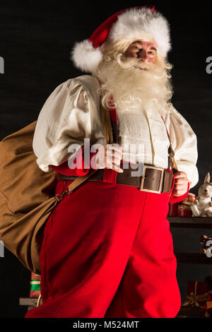 Real Santa Claus carrying big bag full of gifts, at home near Christmas Tree Stock Photo