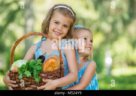 Two little girls holding basket of organic food - bread and vegetables, outdoors Stock Photo