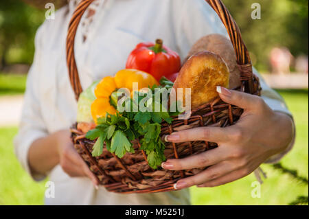 Vegetables in hands. Unrecognizable woman holding basket full of natural organic food - vegetables and bread outdoors Stock Photo