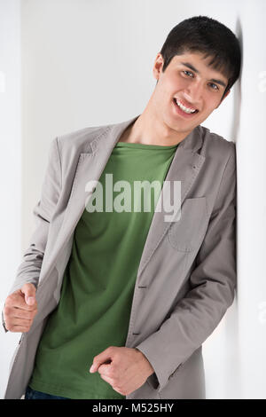Happy smiling young man leaning against white wall Stock Photo