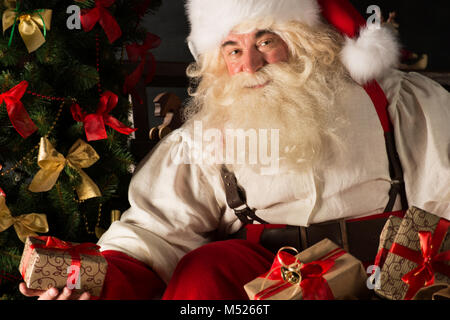 Santa putting gifts under Christmas tree in dark room Stock Photo