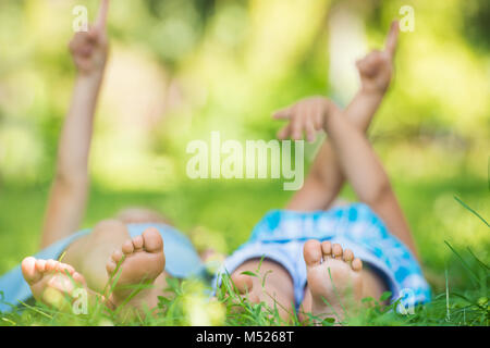 Group of happy unrecognizable children lying on green grass and pointing to the sky outdoors in summer park Stock Photo