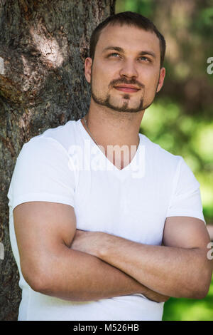 Smiling handsome man outdoors dreaming and leaning on tree. He is confident in his bright future Stock Photo